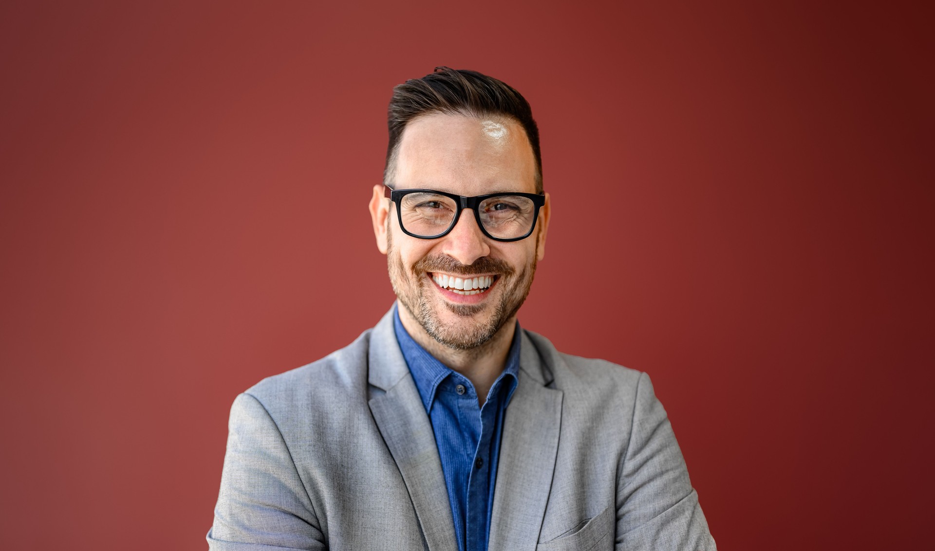 Close-up portrait of smiling young businessman in eyeglasses posing against isolated red background