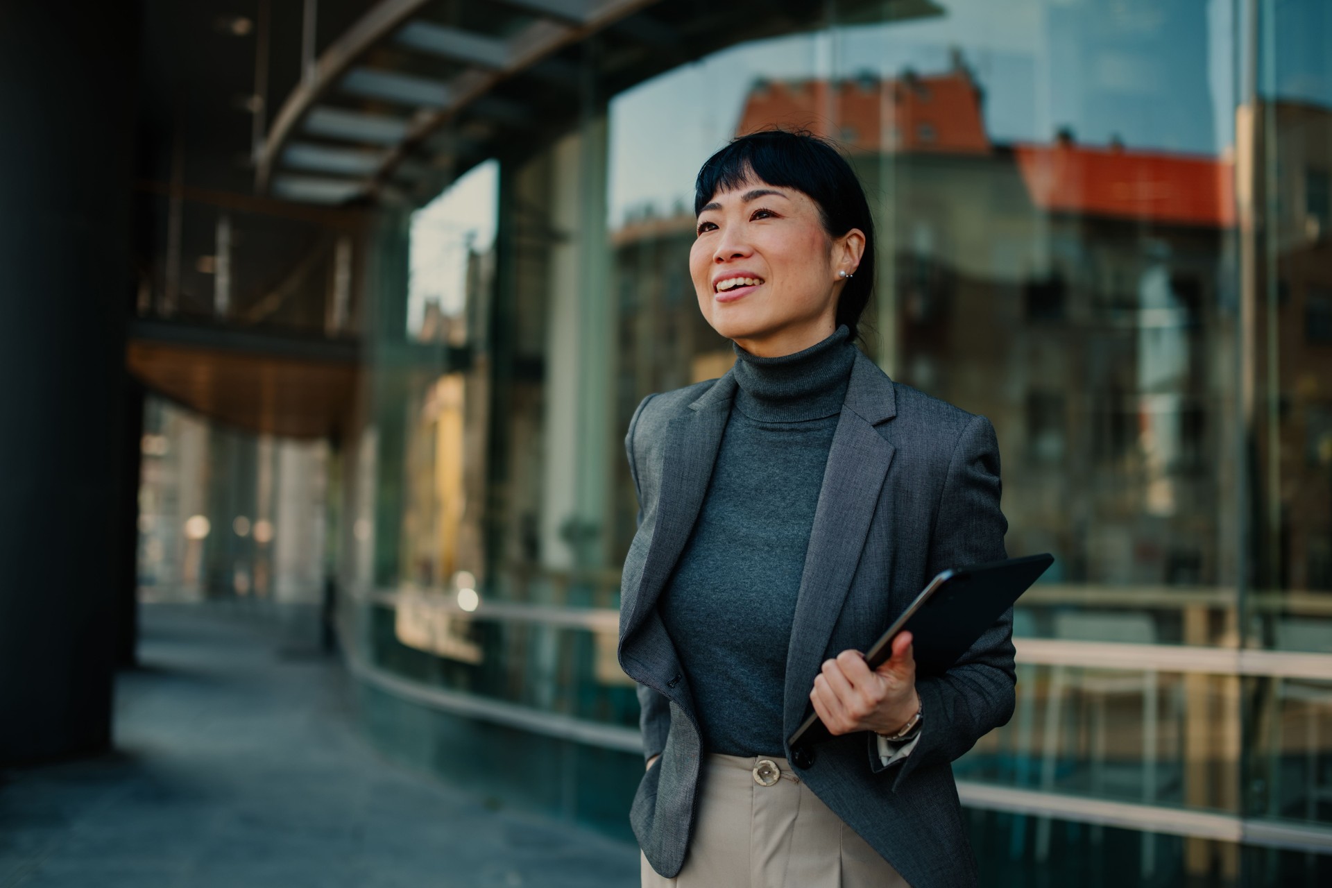 Smiling businesswoman walking outside office building holding tablet
